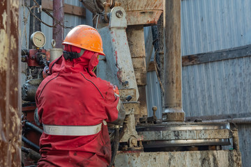 Work driller in red uniform, in helmet and goggles. He uses a hydraulic wrench to screw drill pipes...