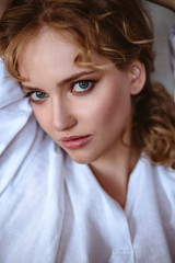Fototapeta premium Young blonde woman in a casual white shirt and jeans in a loft interior, close up fashion portrait