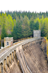 Old dam made in concrete with full lake and pine forest behind, Scotland, UK