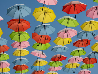Fototapeta na wymiar Bright multi-colored umbrellas soar in the blue sky at noon in the summer heat.