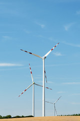 View of a wind power plant on a background of blue sky and fields with grain crops. The concept of environmental electricity production using a wind farm.