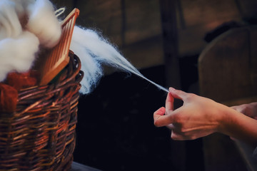 A woman's hand pulls yarn from a wicker basket. Spinner creates a thread of white wool.