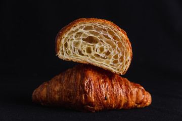 A croissant cut in half on top of a full croissant on black background - 283810083