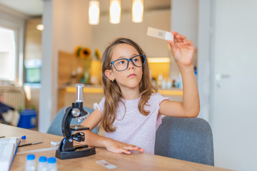 Portrait of Curious Little Scientist. Beautiful elementary schoolgirl uses a microscope for science project. Little girl concentrates while using microscope. Back to school concept.