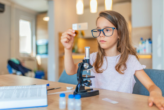 Preschool age girl looks into microscope. Child playing science in the kitchen at home. Cute little girl looking through the microscope. Little girl uses microscope