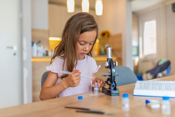 Confident little girl uses microscope at home. Beautiful elementary schoolgirl uses a microscope for science project. Little girl concentrates while using microscope