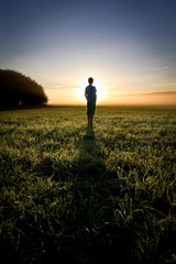 Fototapeta premium Sunrise scene. Silhouette of a boy standing in the field.
