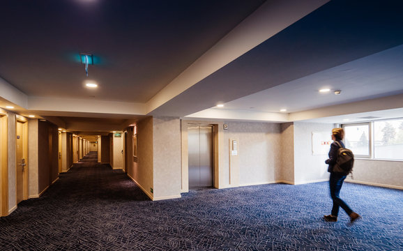 Single Woman Walking Toward Elevator Door And Large Corridor Of Modern Hotel