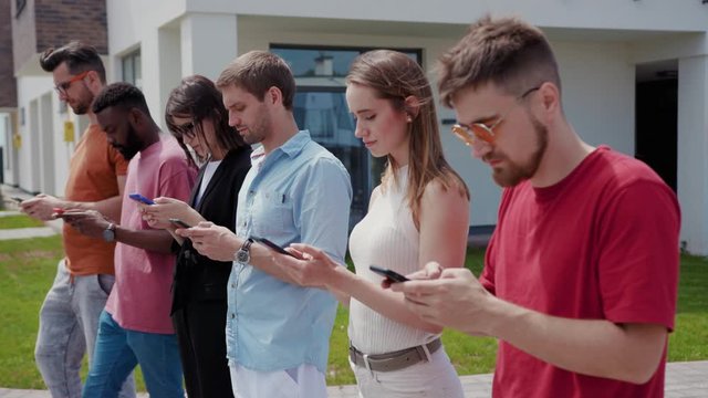 Young people in row using modern mobile phones for online communicatiobn checking social networks news texting message on smartphone.