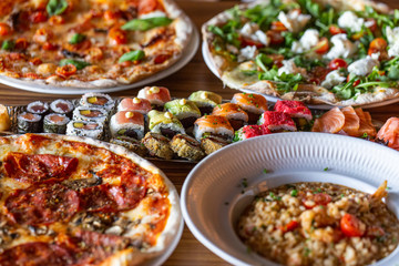 A variety of food on the table in a restaurant made of pizza, sushi. Close-up.