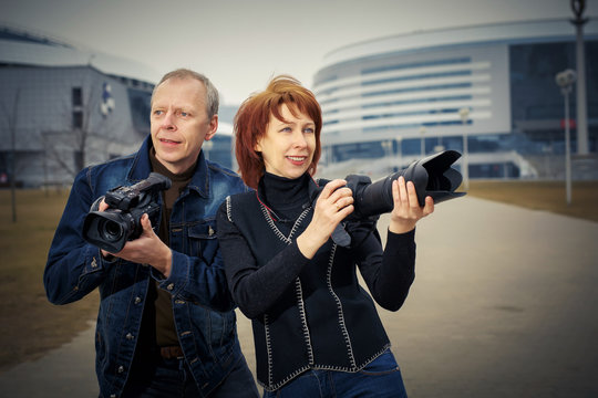 A man and a woman are holding photos and video cameras in their hands.