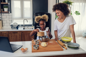 Fototapeta na wymiar Mother Teaching Child to Cook and Help in the Kitchen. African American Mother and Daughter making cookies at home. 