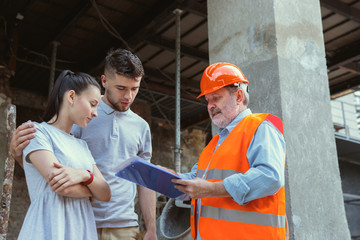 Obraz na płótnie Canvas Foreman or achitect engineer shows future house, office or store design plans to a young couple. Meeting at the construction site to talk about facade appearance, interior decoration, home layout.