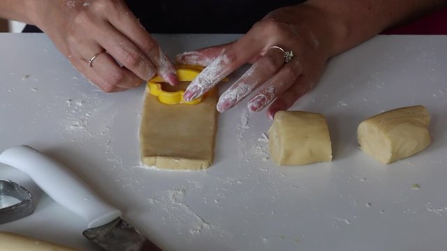 A woman rolls a dough on a table surface with a wooden rolling pin. It makes cookies.