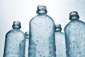 Clear plastic bottles with water drops in monochrome blue white backlit. Concept of global warming, climate change and plastic pollution ocean. Low perspective. 