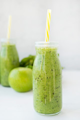 Healthy green smoothie in a bottle on a white table with fresh food. Detox drink for vegetarianism. Vertical orientation.