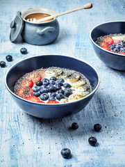 Two bowls of yoghurt and fruits - strawberries, blueberries and banana, cup of honey on blue table. Overhead shot.
