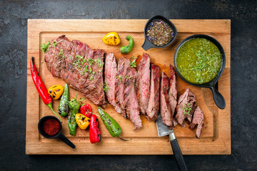 Modern design barbecue dry aged wagyu bavette de flanchet steak with chili and chimichurri sauce as top view on a wooden cutting board