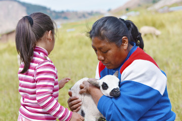 indigenous South American woman with her little daughter taking care of a cute lamb.