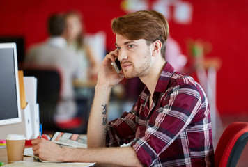 Confident male designer talking on a mobile phone in red creative office space