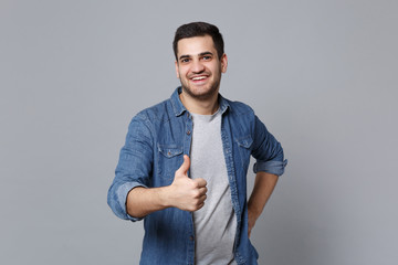 Handsome stylish unshaven young man in denim jeans shirt posing isolated on grey wall background...