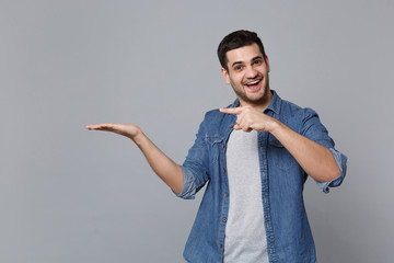 Handsome stylish unshaven young man in denim jeans shirt posing isolated on grey wall background...