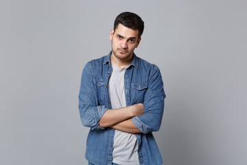 Handsome stylish unshaven young man in denim jeans shirt posing isolated on grey wall background...