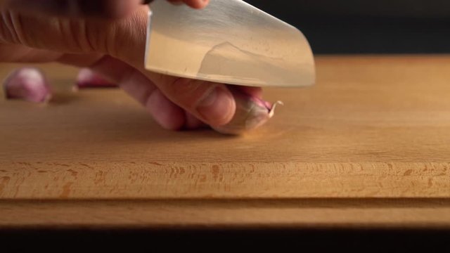The cook cuts the garlic with a knife on a wooden surface. On a black background. Slow motion. Cooking Vegetable Diet Meals