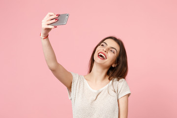 Cheerful attractive young woman in casual light clothes posing isolated on pastel pink wall background studio portrait. People lifestyle concept. Mock up copy space. Doing selfie shot on mobile phone.