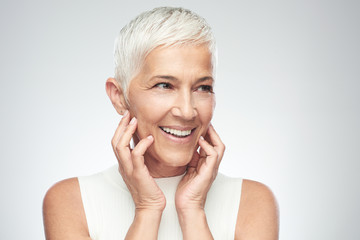 Beautiful smiling senior woman with short gray hair posing in front of gray background. Beauty...