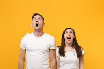 Amazed young couple two friends guy girl in white empty blank design t-shirts posing isolated on yellow orange background. People lifestyle concept. Mock up copy space. Keeping mouth open, looking up.