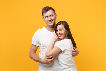 Joyful young couple two friends guy girl in white empty blank design t-shirts posing isolated on yellow orange wall background studio portrait. People lifestyle concept. Mock up copy space. Hugging.