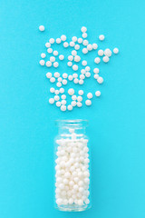 Homeopathic globules in glass bottle on pastel blue background. The globules are scattered from bottle. Alternative homeopathy medicine herbs, healthcare and pills concept. Selective focus, vertical.