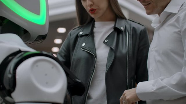 A man and a woman communicate with a cybernetic person smiling and laughing. Robot droid interacts with humans.