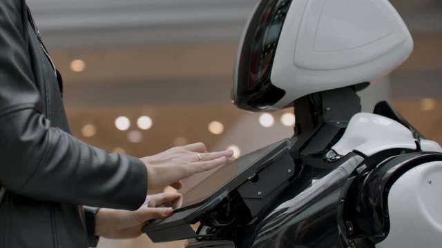Happy woman in contact with cyborg robot. Click on the robot screen. A droid interacts with a woman.