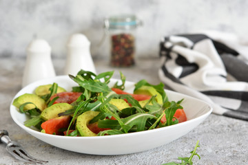 Salad with rucolla, tomatoes, avocado and sauce on the kitchen table. The view is close.