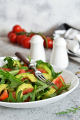 Salad with rucolla, tomatoes, avocado and sauce on the kitchen table. The view is close.