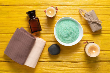 Spa flat lay concept background. Bath salt, aroma oil bottle, soap, towel and black stone on a yellow background.