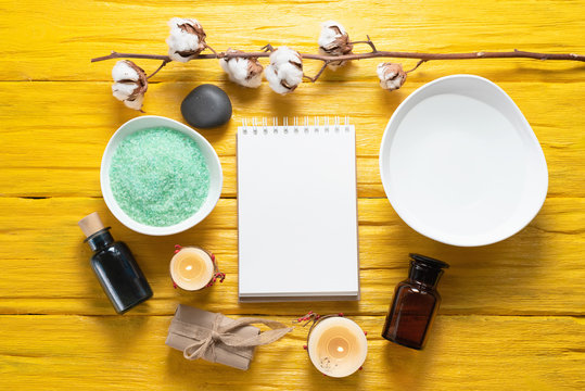 Spa blank page notepad with a copy space mockup. Bath salt, aroma oil bottle and soap on a yellow table background.