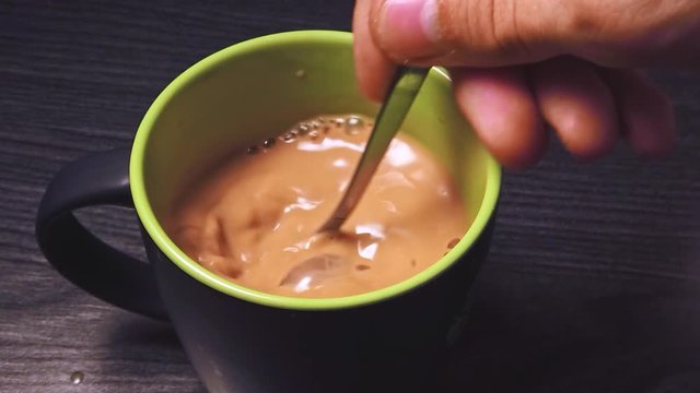 Close-up slow motion of mixing black coffee with milk by a man on wooden table in the kitchen