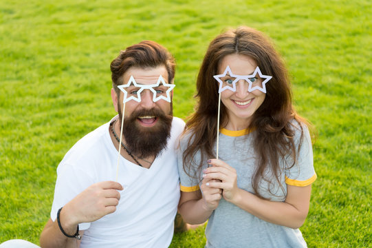 Fun props. Funny couple holding star-shaped photobooth props on sticks. Happy family celebrating with party props. Bearded man and sensual woman smiling with fancy props on green grass