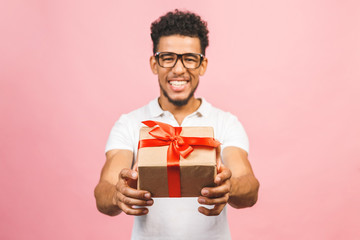 Cheerful smiling african american millennial guy in eyewear holding wrapped present box. Happy black young man congratulating, giving birthday gift, isolated on pink background.
