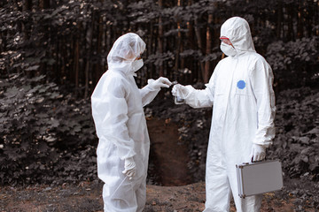 Ecological problem. Pollution. Examine soil. Scientist working in forest in protective mask and suit taking water and soil samples. Chemist makes an analysis of the environment for radiation. 
