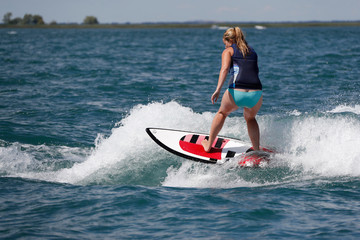 Woman riding a surfboard on a boat wake.