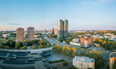 Obraz premium Panoramic, aerial view over Riga city. Modern buildings, roads, and other infrastructure. Cable bridge leading to iconic old town panorama in vivid sunset colors. 