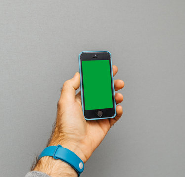 PARIS, FRANCE - OCT 4, 2017; Man holding iPhone 5 SE smartphone against grey background in blue leather protection cover with green chroma key