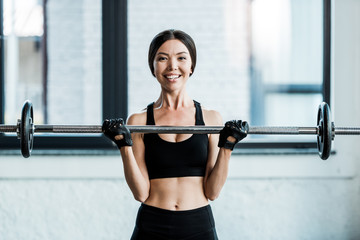 Fototapeta premium cheerful woman working out with barbell in gym