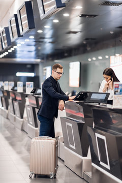 Business Trip. Handsome Young Businessman In Suit Holding His Passport And Talking To Woman At Airline Check In Counter In The Airport