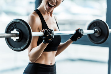 cropped view emotional young woman working out with barbell in gym