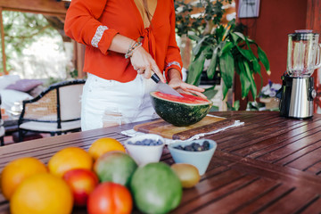 young woman preparing a healthy recipe of diverse fruits, watermelon, orange and blackberries. Using a mixer. Homemade, indoors, healthy lifestyle